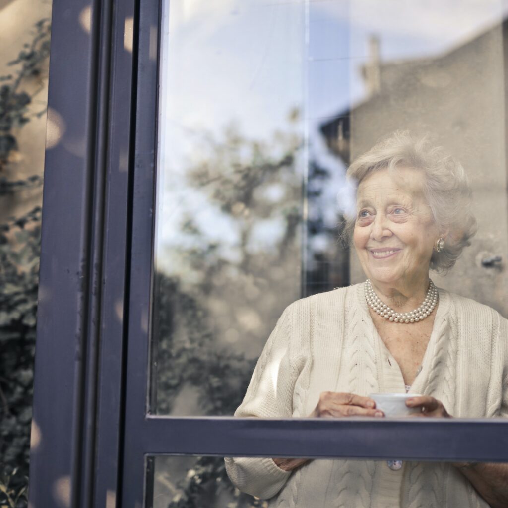 Photo: Older woman looking out of a window, smiling