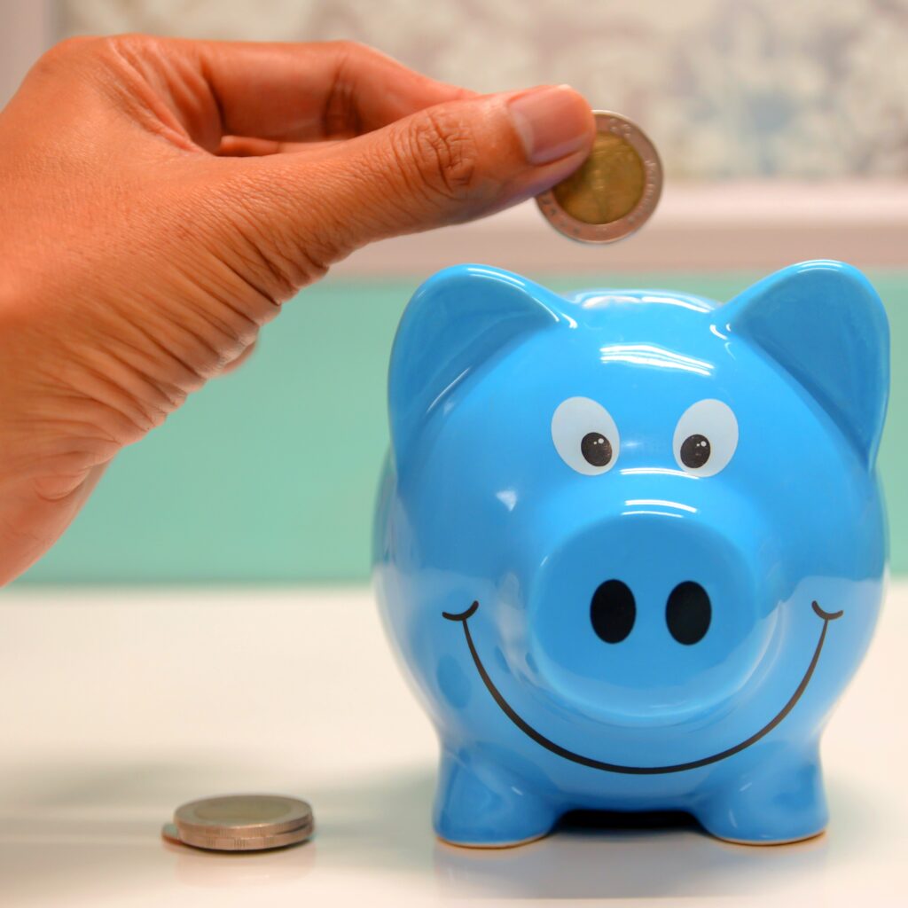 Photo: hand putting a coin in a piggy bank